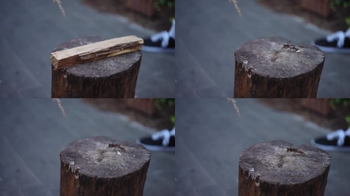 特写镜头。一个男人站在户外，正试图用斧头砍一块躺在圆木上的木头。劈柴生火。用放在圆木上的斧头劈木头。