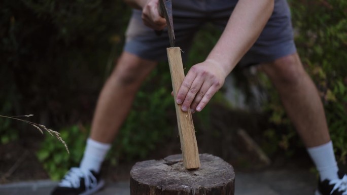 特写镜头。一个人用斧头把立在圆木上的木头劈成碎片。劈柴生火。用放在室外圆木上的斧头劈木头。准备柴火。
