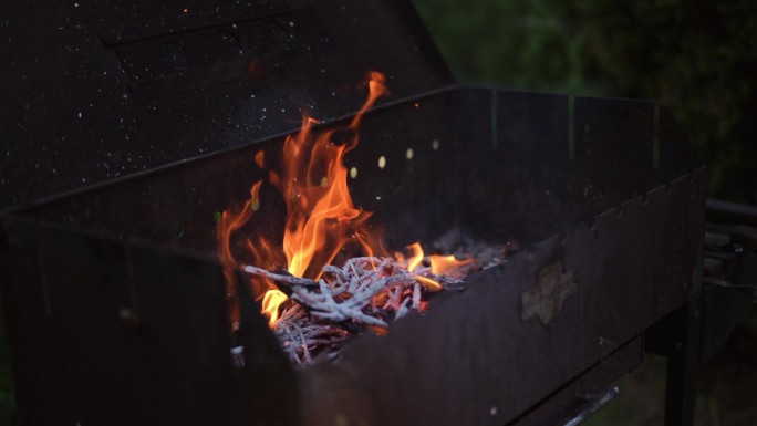 特写镜头。从燃烧的干树枝和灌木中，把木炭从纸袋里撒到烧烤架上。
