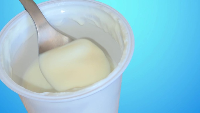 勺子沉入白色酸奶罐，蓝色背景的概念，健康食品和饮食