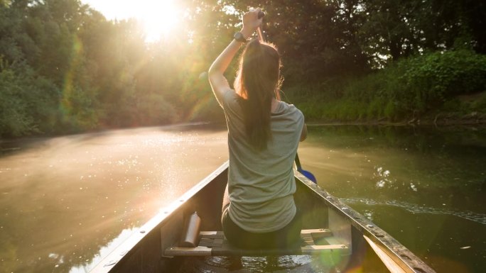 日落时分，一名女子划着独木舟探索一条美丽的河流