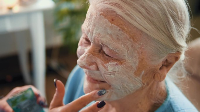近距离拍摄的微笑的老妇人在80年代使用粘土面膜护肤和面部年轻化