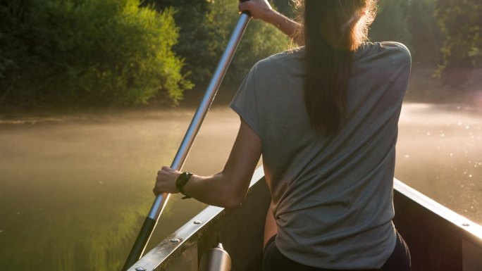 活跃的年轻女子在黄昏时在薄雾笼罩的河流上划着独木舟
