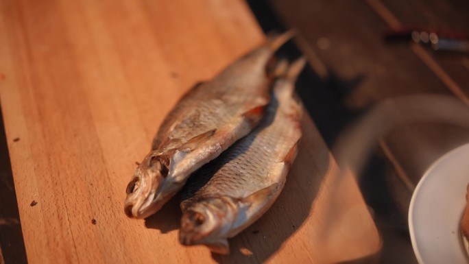 特写镜头。木板上放着两条咸咸的干腌鱼。一个男人的手把另一条鳕鱼放在板上。