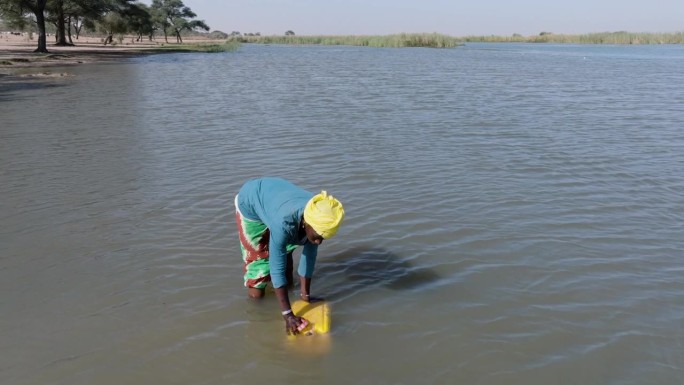 天线。黑人妇女从被污染的塞内加尔河中装水。萨赫勒，撒哈拉沙漠，北非。干旱，气候变化，沙漠化