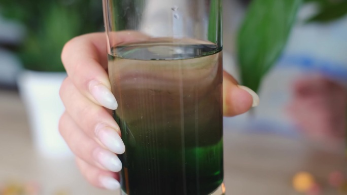 一个女人拿着一杯叶绿素，促进身体健康。从维他命、矿物质和叶绿素的混合中开始你的一天，这是一个健康的早