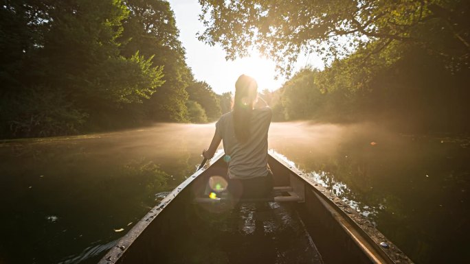 一个女人划着独木舟，在雄伟的雾蒙蒙的河流中探险