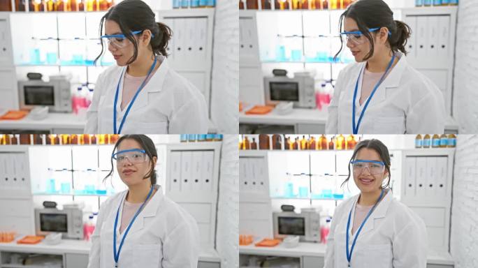 一个微笑的年轻西班牙妇女穿着实验室外套和防护眼镜自信地站在设备齐全的现代化实验室里。