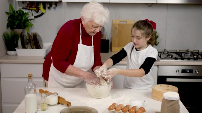 系着围裙的女人和成年女孩一起在厨房做饭。老奶奶和孙女在做馅饼。享受过程。将技能代代相传