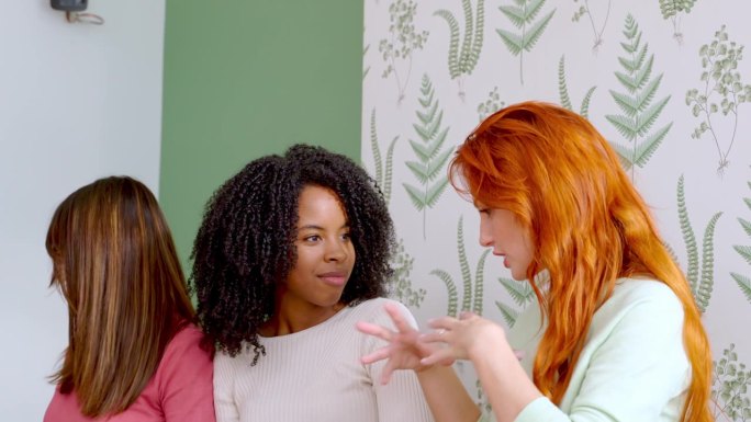 三个女人在一个贴着植物墙纸的房间里聊天。