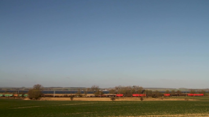 红色火车穿过乡村风景，天空湛蓝，白天的广角镜头