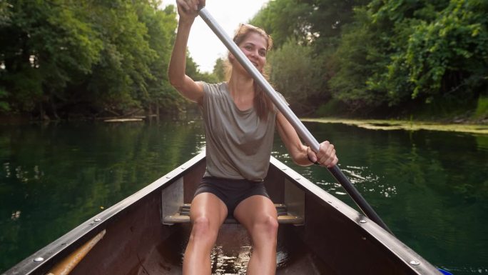女子在郁郁葱葱的绿色大自然中划独木舟探险