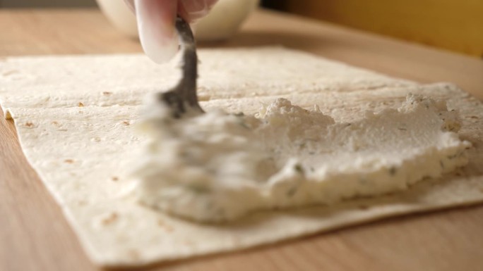 在展开的皮塔饼上放上一层奶酪馅。皮塔饼卷的制作。