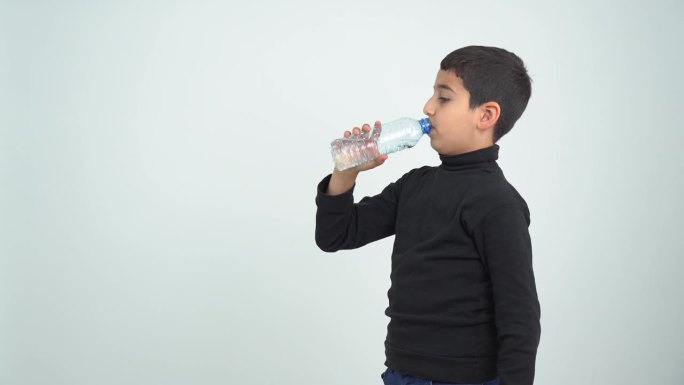 一个孩子愉快地从一个成年人手中接过一瓶矿泉水，喝了下去，孤立在灰色的背景中