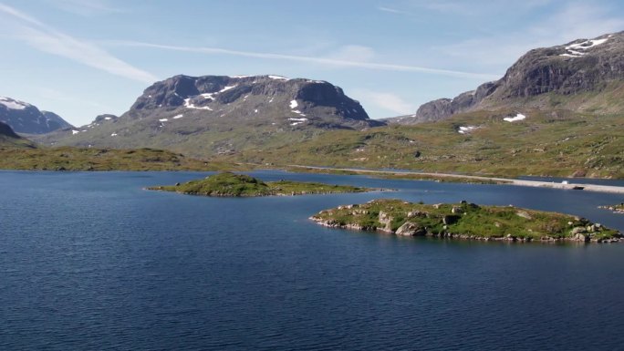 鸟瞰挪威峡湾的一系列小岛。一条长长的马路穿过风景，上面停着一辆白色货车。远处可以看到白雪皑皑的青山。