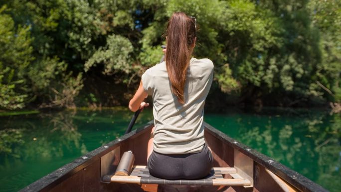 年轻女子在平静的绿色河流上的独木舟上放松