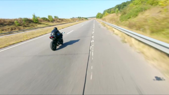 空中拍摄的男子骑着现代运动摩托车在高速公路上在夏天的一天。摩托车手在乡间公路上驾驶摩托车。有人在旅途