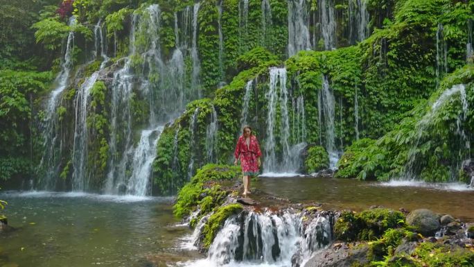 一名女子站在巴厘岛清新的瀑布旁
