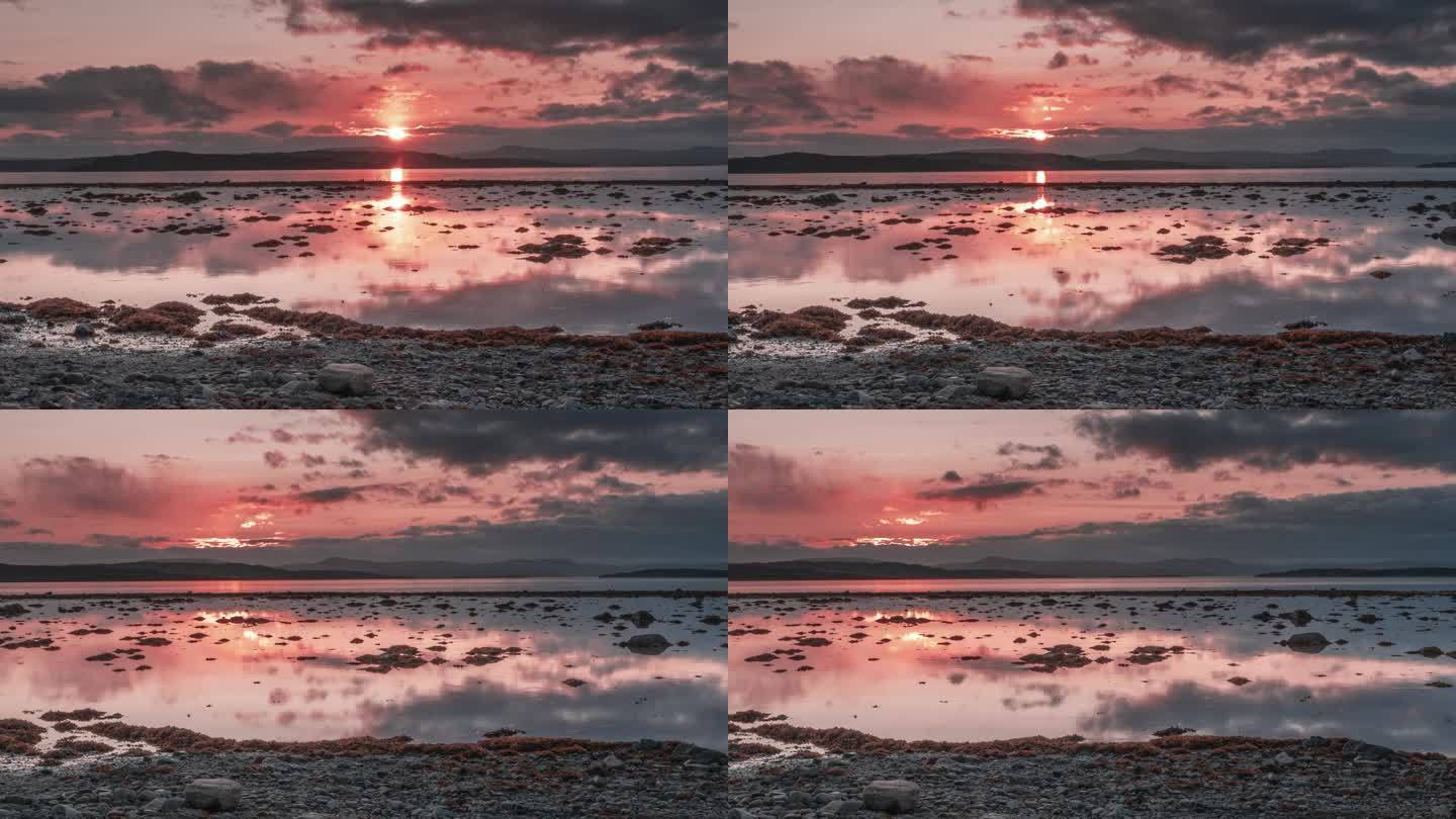 火红的晚霞和黑云倒映在平静的峡湾水面上。退潮时露出长满海藻的沙洲。