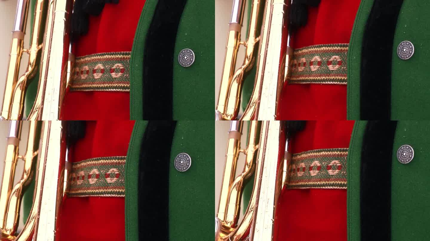 男子民族服装的上半身，一件厚厚的绿色上衣，一件红色针织背心和绣花皮裤吊带，手持长号