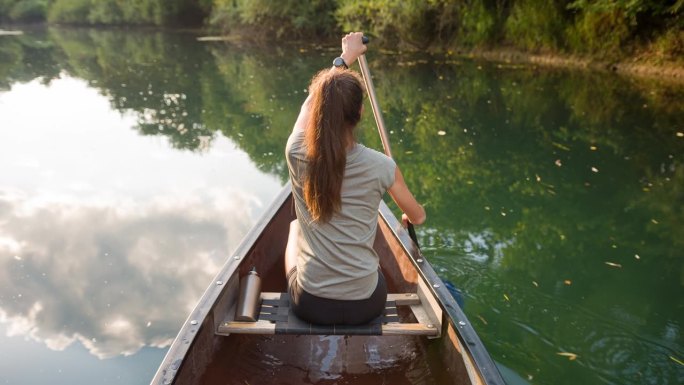 年轻女子在平静的河上划着独木舟休息