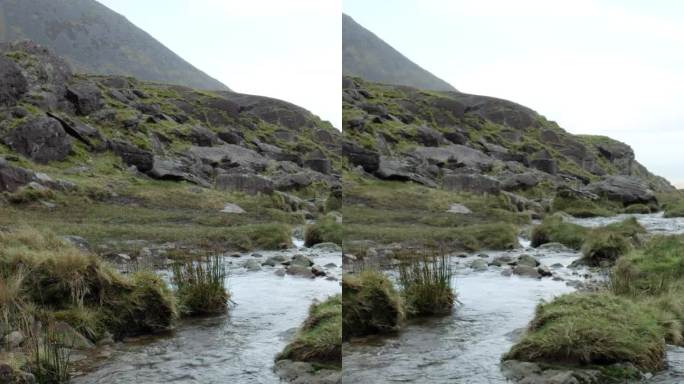 一条清澈的山间溪流在布满岩石的环境中流动，以云彩为背景。垂直视频，平移。