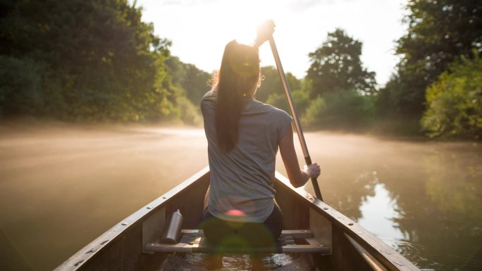 日落时分在荒野中划着独木舟的年轻女子