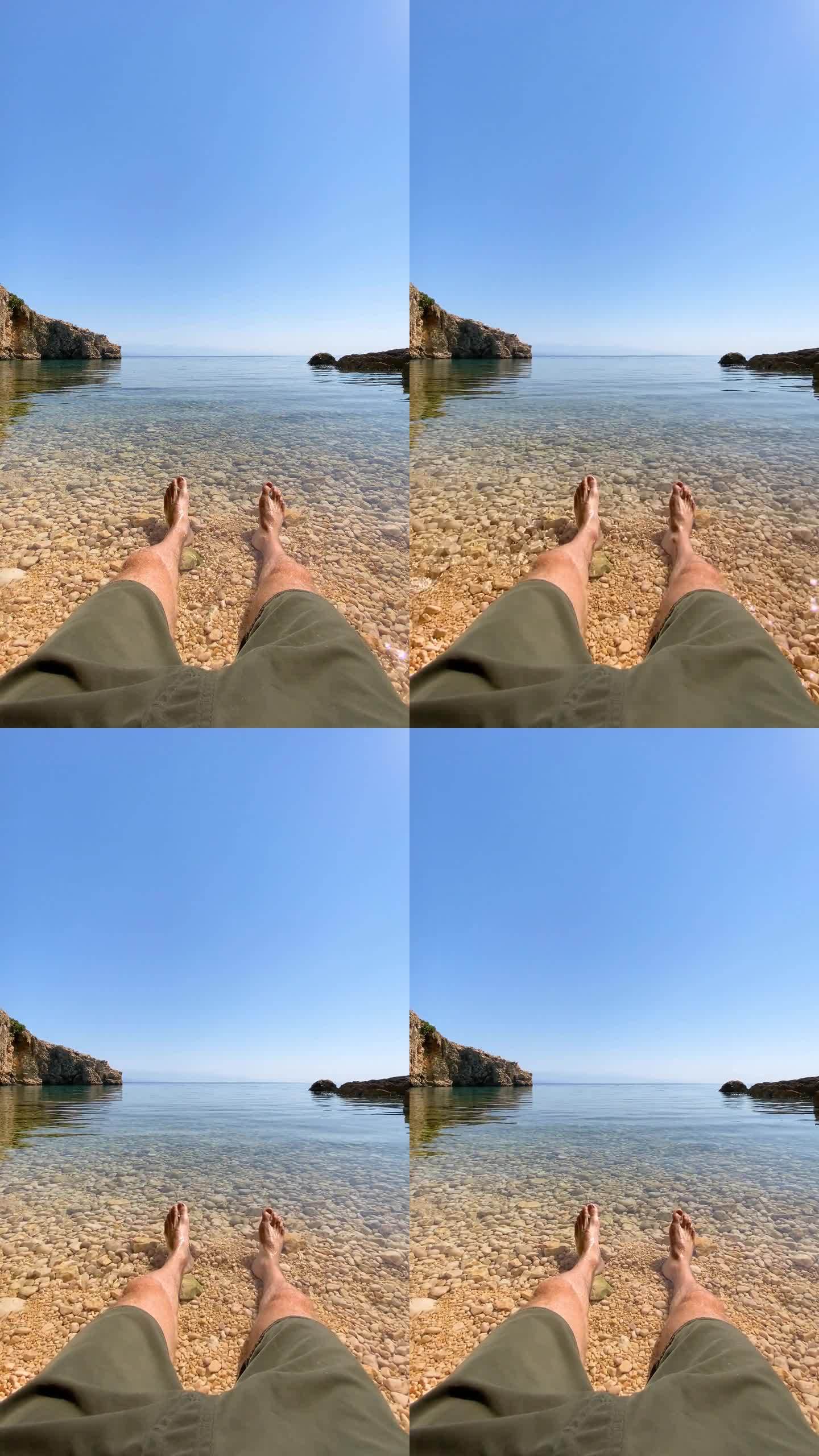 男子在沙滩上放松，双腿伸入大海，POV