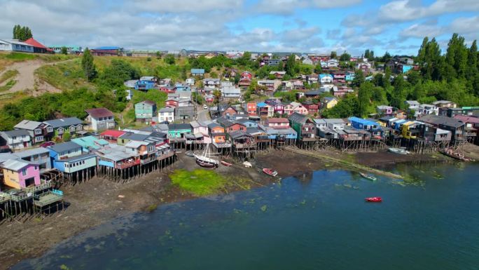 空中无人机高脚楼彩色村庄在岛海chilo<e:1>智利巴塔哥尼亚旅游目的地建立拍摄，绿色的小岛山丘与