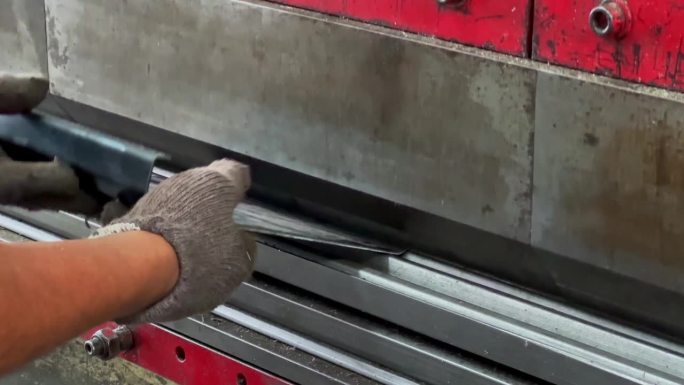 操作员使用折弯机在铁板上压痕的特写镜头。手戴布手套，握着折弯机上的铁板
