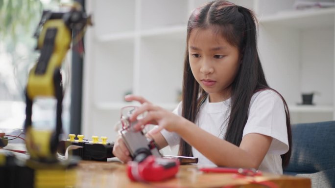 年轻的亚洲女孩在她的平板电脑的在线教程的帮助下学习组装汽车机器人