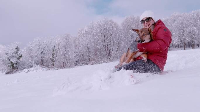 一位微笑的女士抱着她可爱的狗狗在新下雪的雪地上滑雪