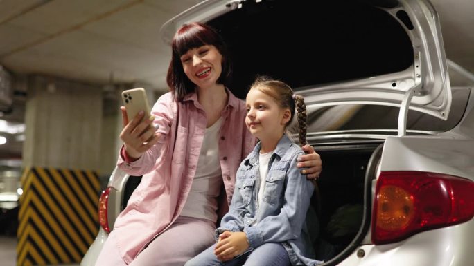 母女俩在地下停车场用智能手机自拍。