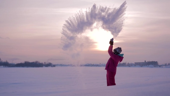 在一个美丽的冬日，日落时分，女孩在寒冷的空气中泼热水。慢镜头