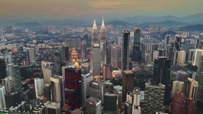 傍晚时分吉隆坡市中心的航拍照片，马来西亚。在吉隆坡，飞机飞过灯火通明的摩天大楼和山丘