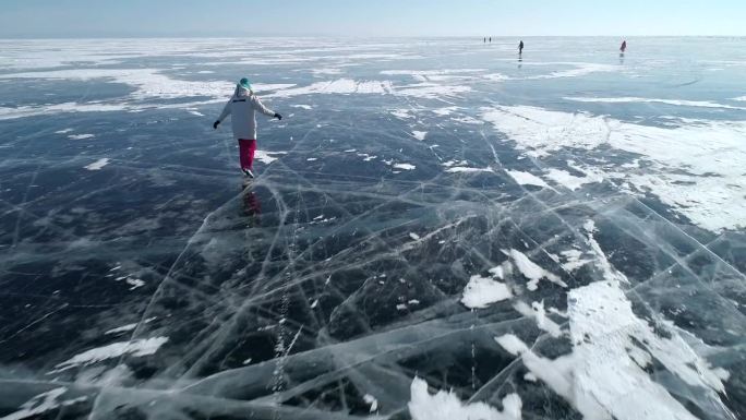 航拍的女孩在贝加尔湖冰封的蓝色透明冰面上滑冰，冰面上有裂缝。自然地标。冬天的风景。热门旅游目的地。慢