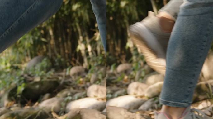 垂直视频。穿着运动鞋的女人们踩着滑溜溜的石头过河。她走进一片竹林。