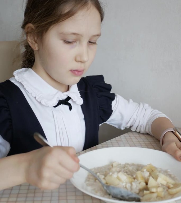 一个穿制服的女学生在放学或上学前吃燕麦片和香蕉的特写。一个十几岁的女孩早餐或午餐吃粥。学校健康饮食的