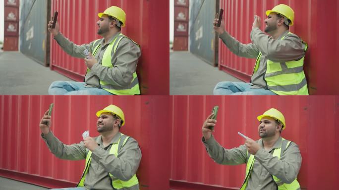 年轻的工业工程师在集装箱堆场辛苦工作后，一边用智能手机视频通话，一边展示美元钞票。日工资，美元钞票的