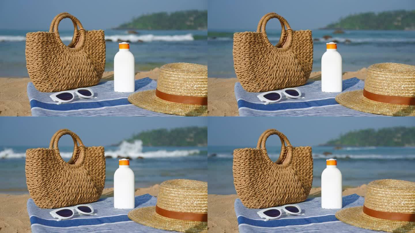 沙滩上的沙滩必需品:一瓶防晒霜，时髦的草帽，毛巾上的遮阳帽，旁边的柳条手提袋。热带海岸夏季皮肤防紫外