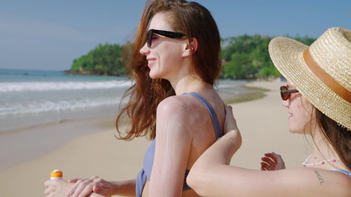 一名女子在沙滩上给自己的手涂防水防晒霜。快乐的女孩们在海边涂上防水防晒霜。使用防晒系数进行日光浴的女