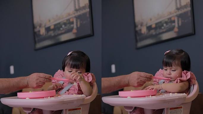 女孩坐在椅子上吃东西，因为没有胃口，扔掉了食物，而她的爸爸试图用勺子喂她