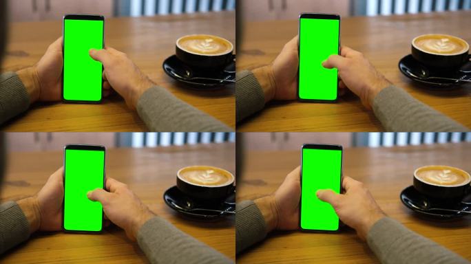 一个年轻人坐在咖啡馆里，手里拿着绿色的智能手机模型屏。男性使用色度键手机。垂直模式。触摸，滑动显示屏