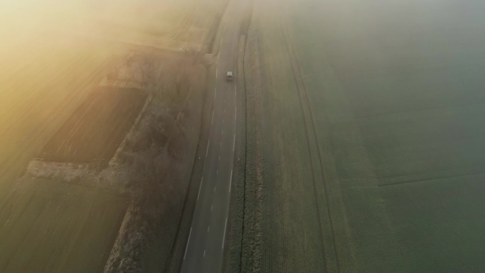 鸟瞰图:汽车在绿色的田野上滑行，被柔和的雾包围