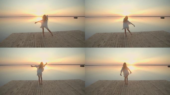 身穿白裙的金发女子在湖边的木码头上跳舞，夕阳西下