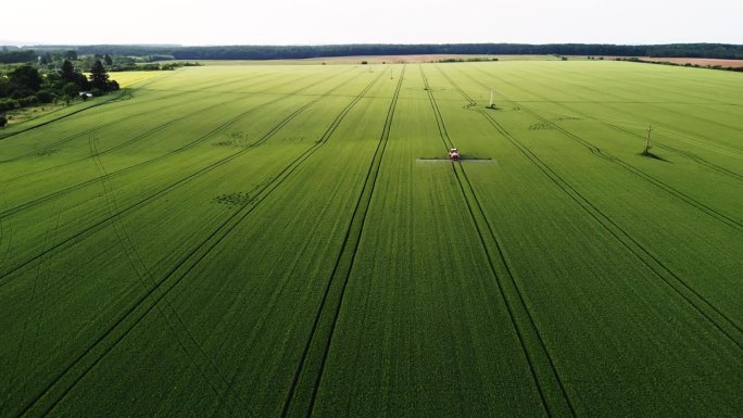 无人机空中交响乐:拖拉机在日光下喷洒绿色的田野，在农业进步的挂毯上