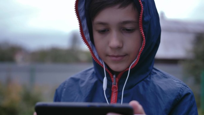 都市逃避主义:穿着卫衣的男孩在街上，沉迷于手机里的音乐