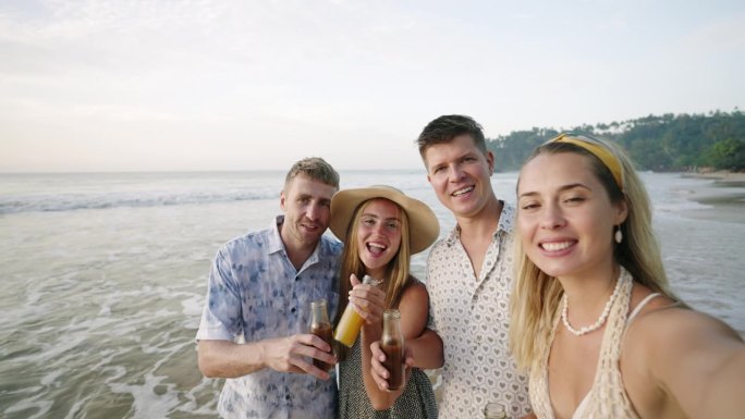 有趣的朋友群男人，女人拿着一瓶柠檬水在相机前摆姿势，自拍，在阳光明媚的热带海滩上欢呼。两对兴高采烈的