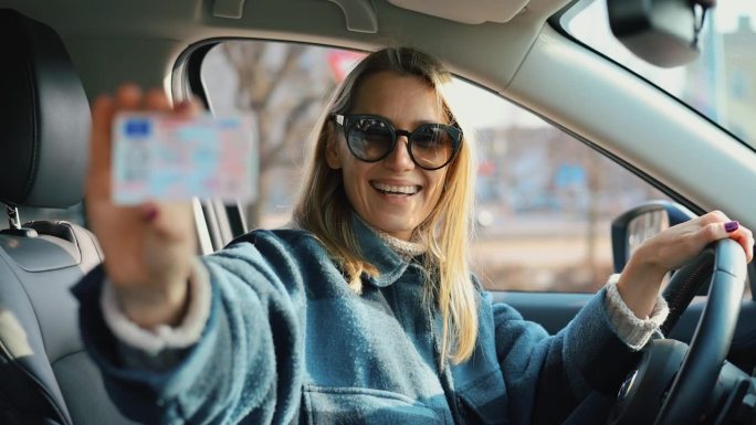 快乐的女人坐在车里，展示她的新驾照