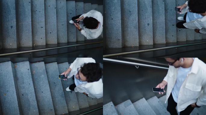 俯视图:一头卷发的年轻白人男性在室外楼梯上沉迷于使用智能手机。